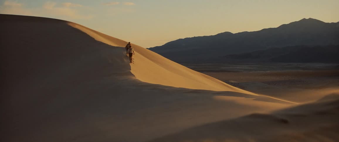 Two men walk on a sand dune in the desert under the hot sun