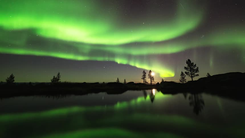 Northern lights in the moonlit night sky over a serene lake