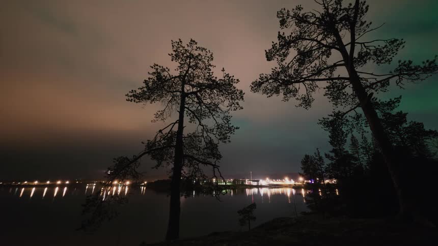 A bright lit town in the distance with clouds and auroras above