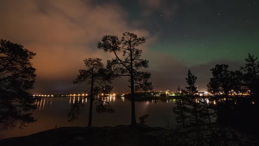 Northern Lights behind clouds over city lights and reflections