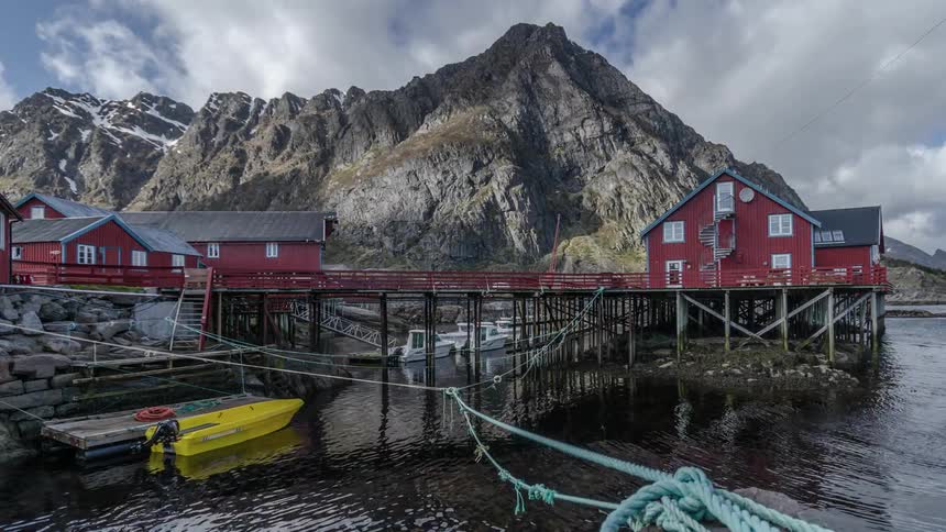 Timelapse of ropes and a small boat floating next to a dock with a mountain in the background