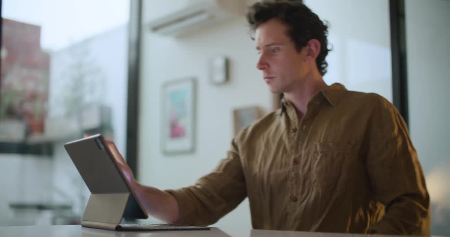 A man taps and zooms in on a tablet screen while sitting at home
