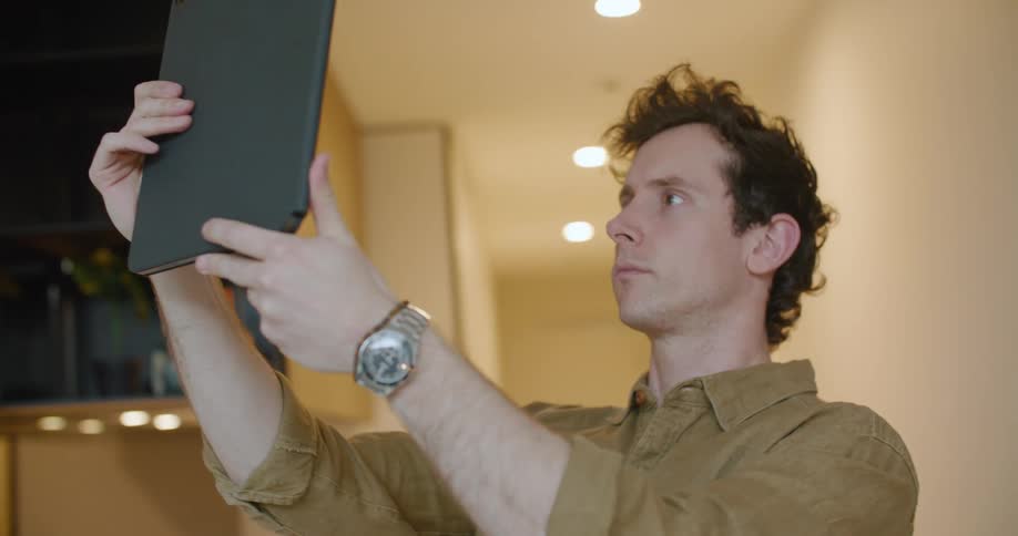 Man with brown shirt and grey watch uses tablet with case