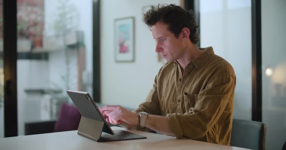 Man sits at a table and uses the touchscreen on a tablet that has an attached keyboard