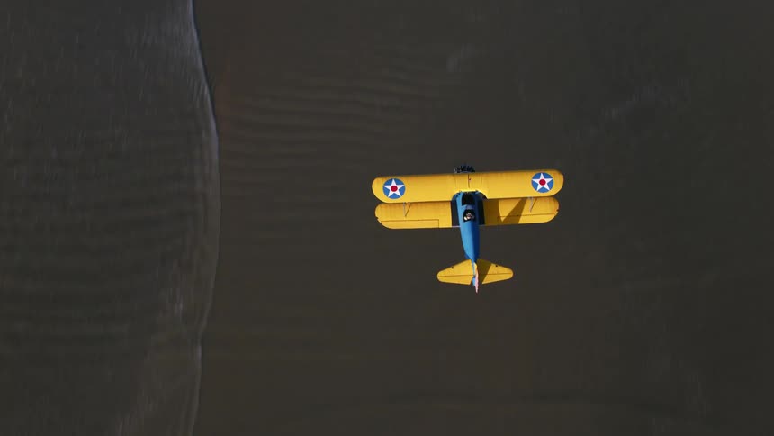 An airplane flying in the air over a beach with waves of water and sand
