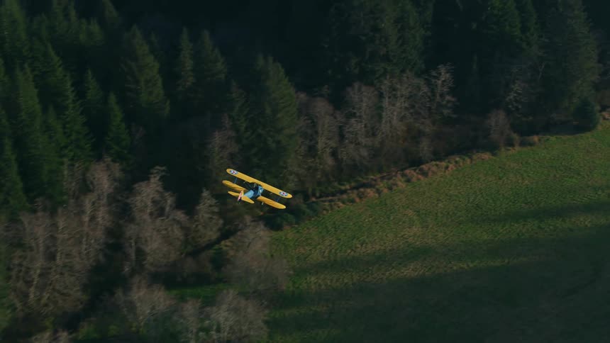 A biplane flies low in the sky and not far from the expansive forest below