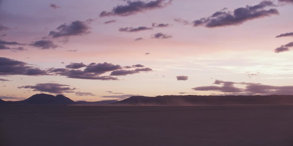 A desert would sand with a mountain range the sky and clouds in the background