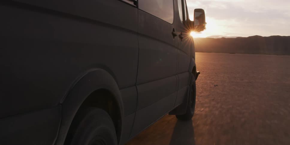 A van driving on the smoot desert soil near the mountains at sunset