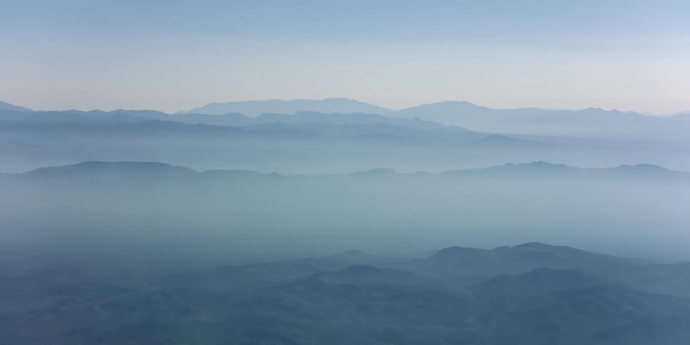 An extensive mountain range is shrouded in a dense layer of fog on a bright day