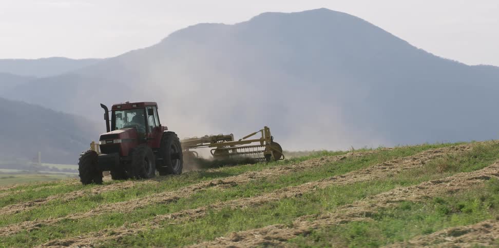 A tractor plows a farm with mountains in the distance