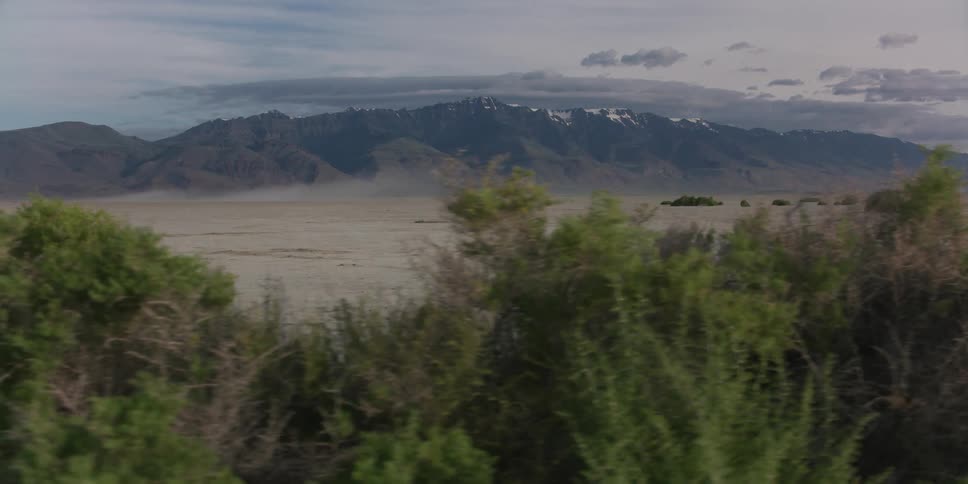 A landscape with shrubs with a mountain range the sky and clouds in the background