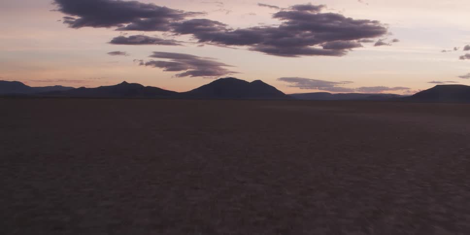 As the sun is just below the horizon a dry and arid landscape is revealed and mountains are seen in the distance