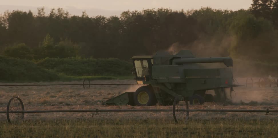 A harvester in a field with trees the sky and clouds in the background
