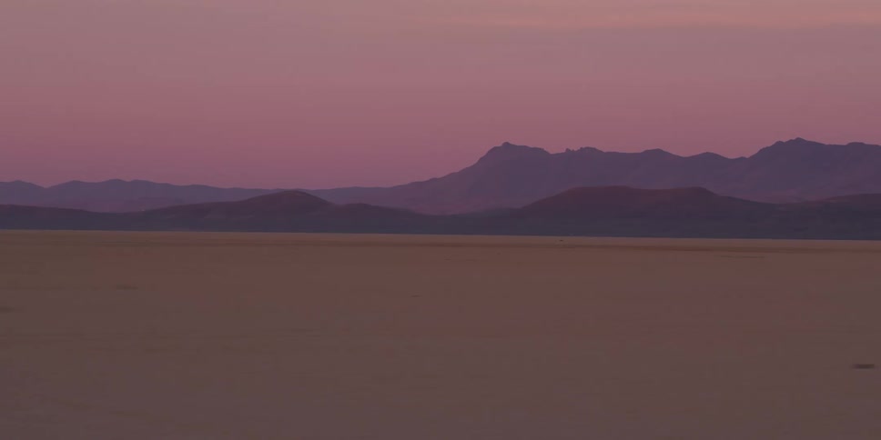 Sandy flat lands with the silhouette of jagged ridge at sunset