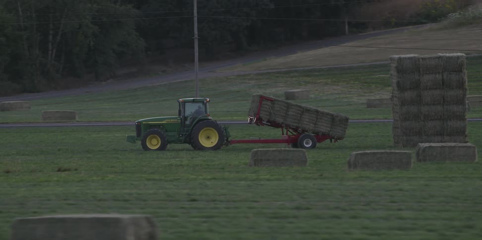 A tractor sits in a field with bales of hay