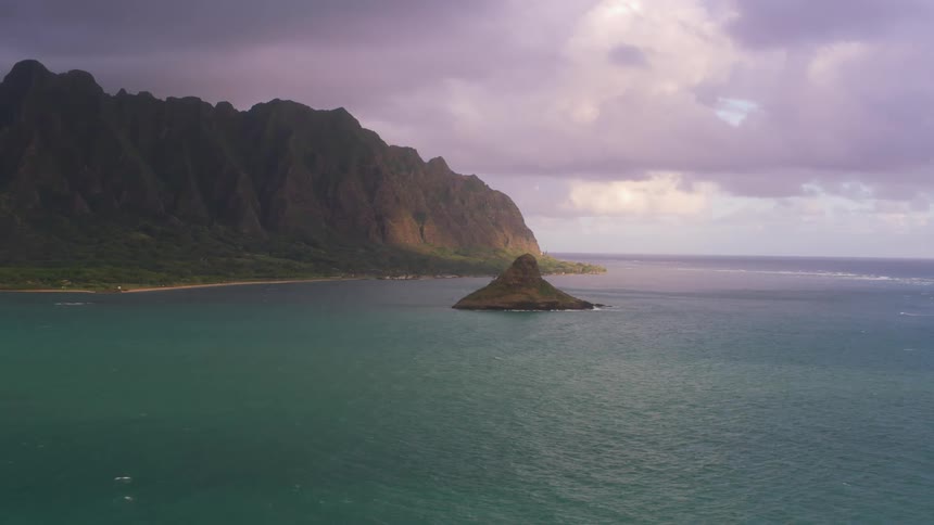 A coast with a cliff and island with the sky and clouds in the background