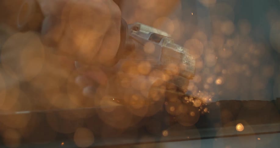 Shower of yellow sparks when a man uses a power tool to grind metal