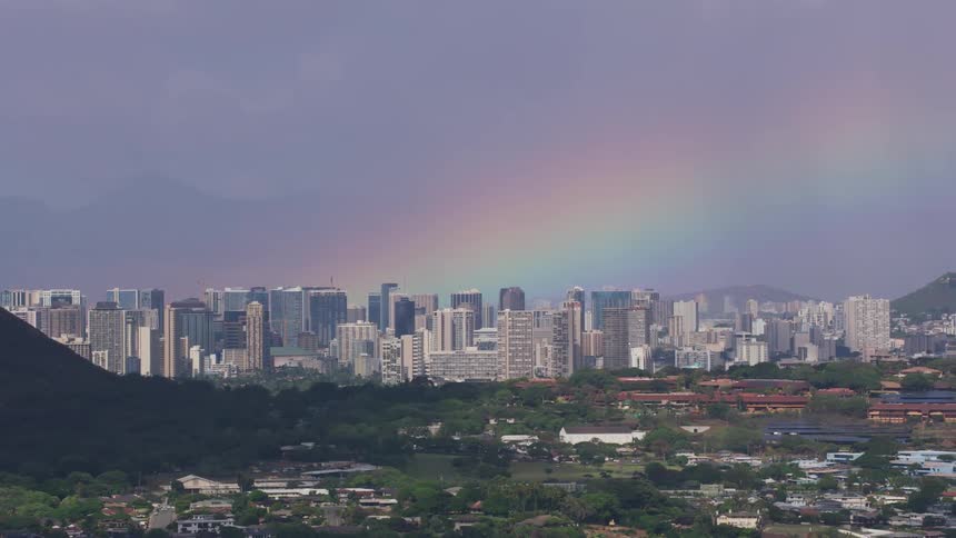 A city skyline with the coast in the foreground with a rainbow the sky and clouds in the background