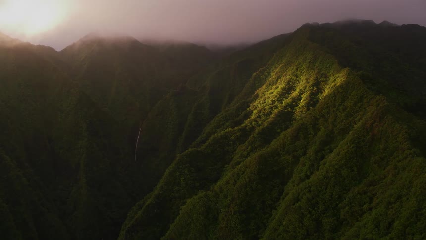 The sun glows through the heavy clouds onto green lush ridges