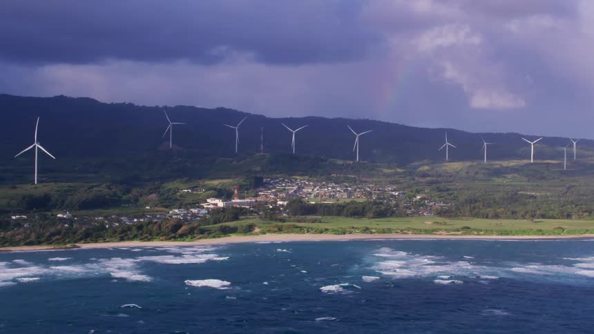 Wind turbines sit behind a neighborhood along the coast