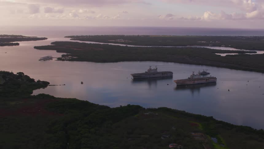 Ships float mid river bordered by forest close to town under cloudy sky