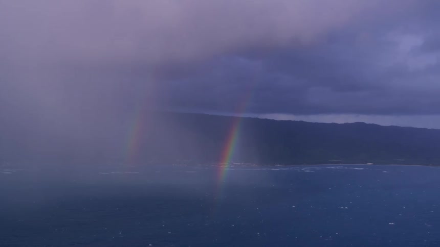 Aerial view of a double rainbow over the rain falling over the ocean near the mountains