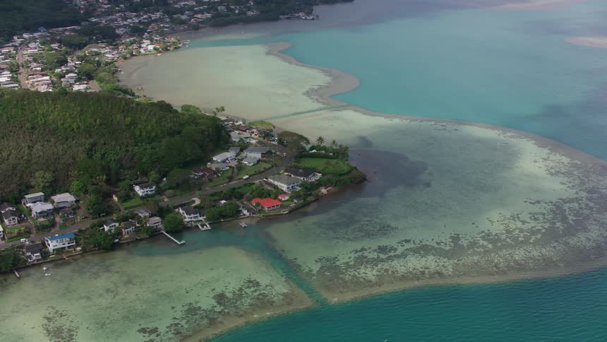 Sandy beach and pale blue water surround buildings sitting between forest and shore