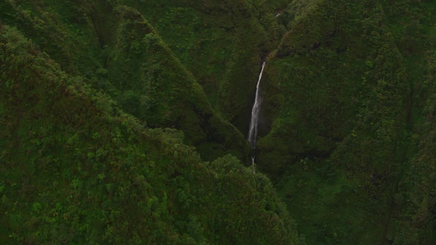 A long slender waterfall pours down between mountains covered in thick vegetation