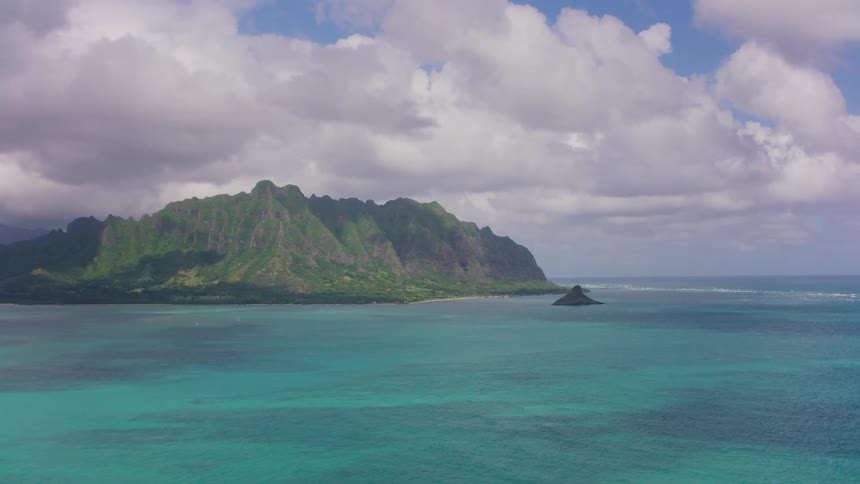 Aerial view of an islet in the ocean in front of the coast near the mountains