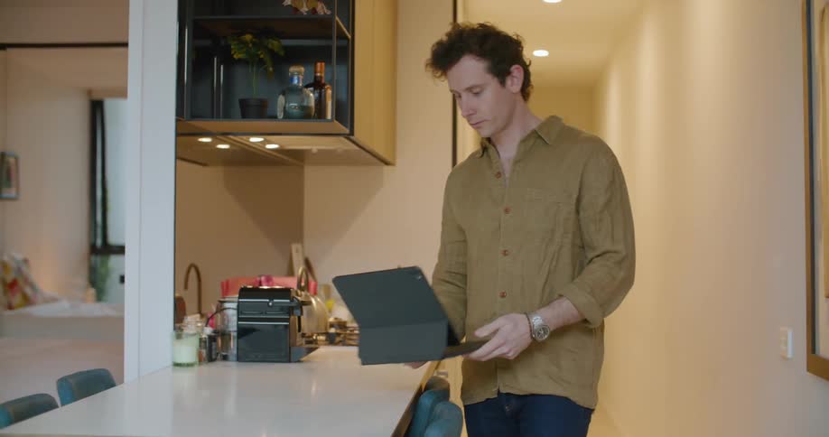 Man sets up laptop and places it on kitchen counter as he looks around before swiping at screen