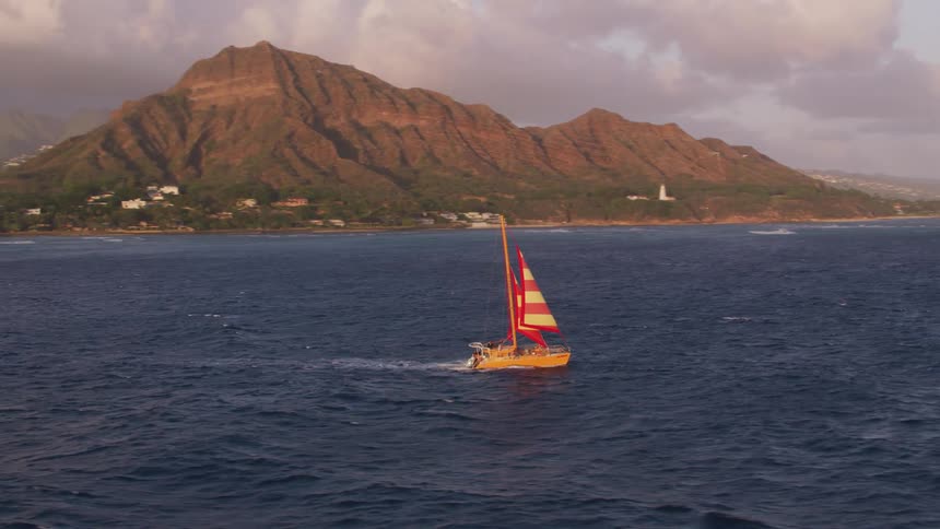 A small sailboat moves swiftly over the ocean water near a coastal city