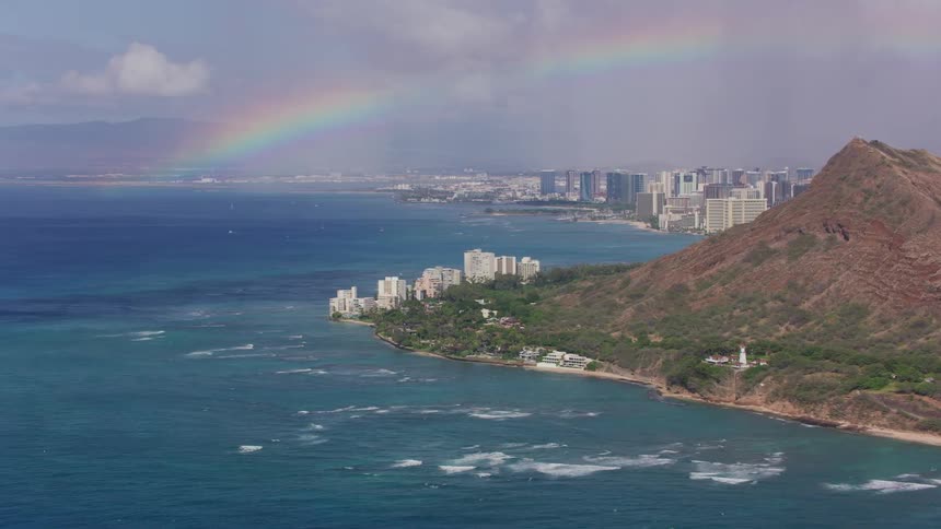 Waves rolling in along the coast as a rainbow stretches across the sky