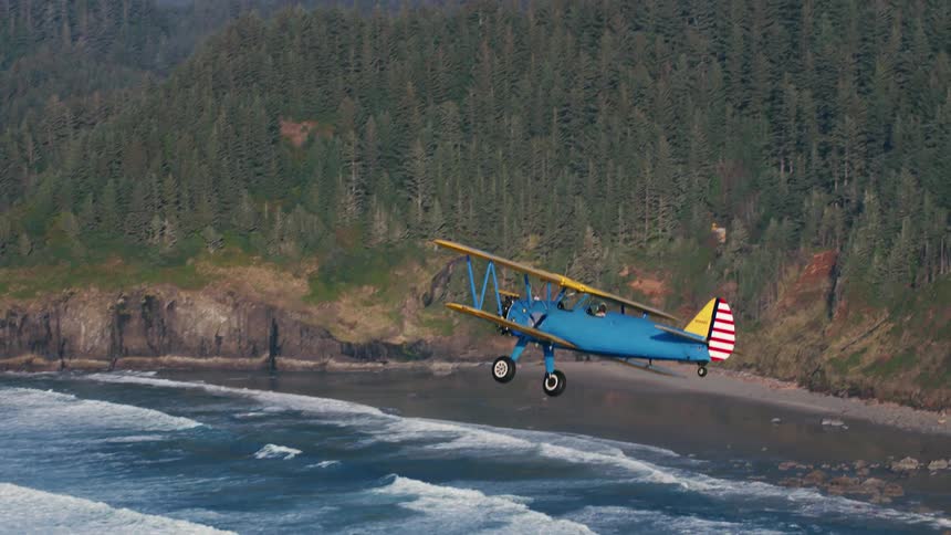Fog covers forest and mountains as biplane flies over waves and rv drives along highway bordered by fence