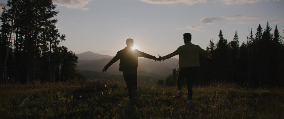 Young couple running on the hill holding hands in front of the sunset