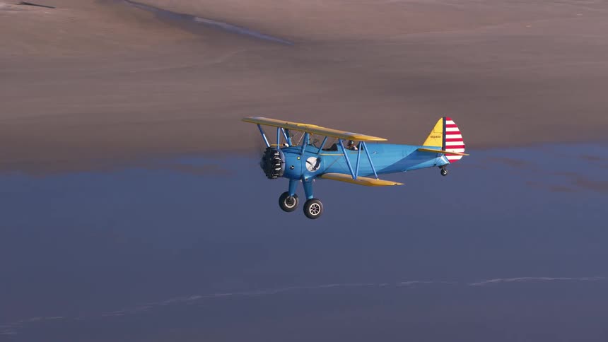 Yellow and blue biplane flying over a beach at daytime