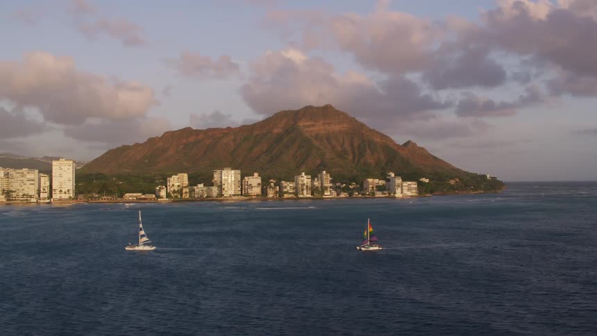 A pair of saul sailboats make their way over the ocean near a coastal city