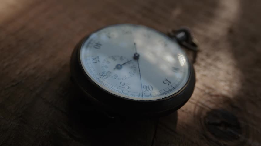 A ticking pocket watch lies on a wooden tablet