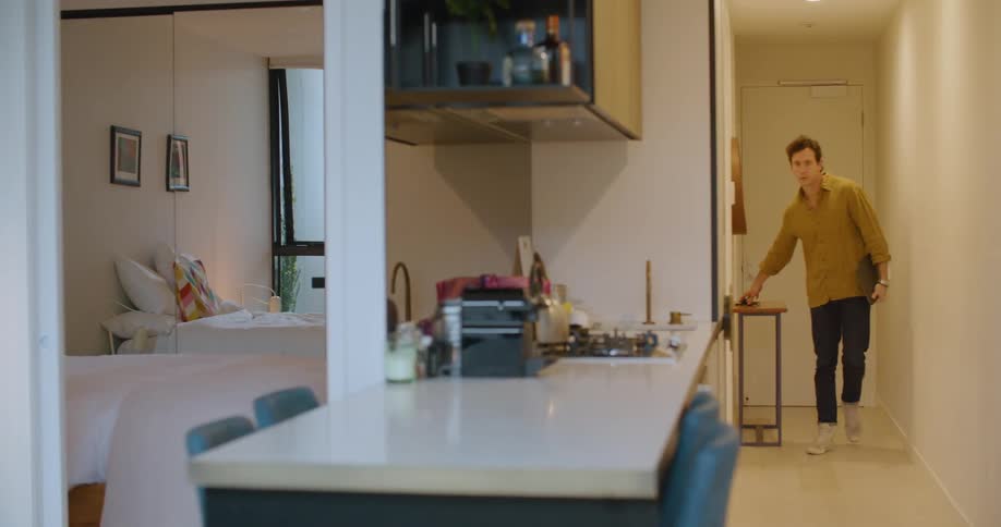A man with a laptop opening a door and entering a room with a wall in the background
