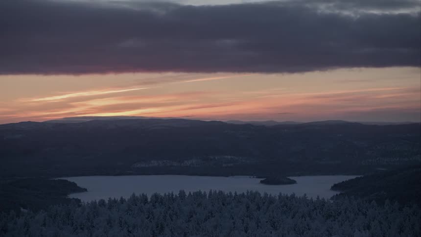 A small frozen lake at sunset surrounded by hills and trees
