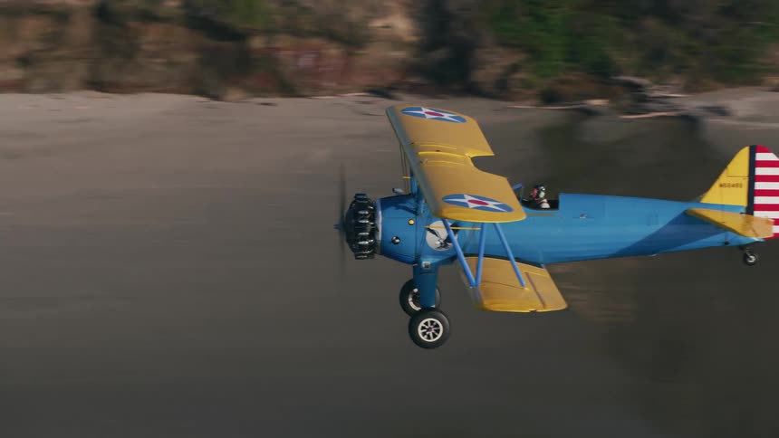 A man flying a biplane along the coastline