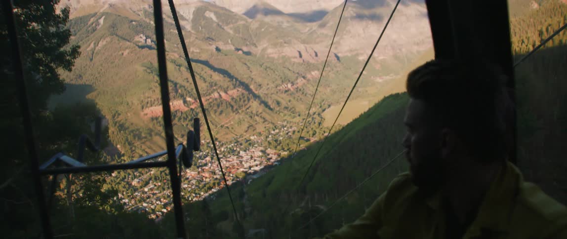 Man looking out the window of a cable car going up the mountain near a small town