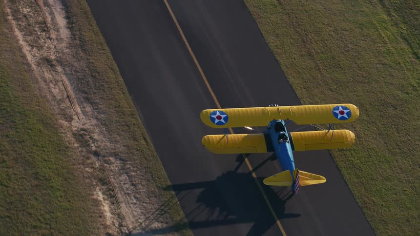 Colorful yellow and blue biplane moves down runway between mowed fields