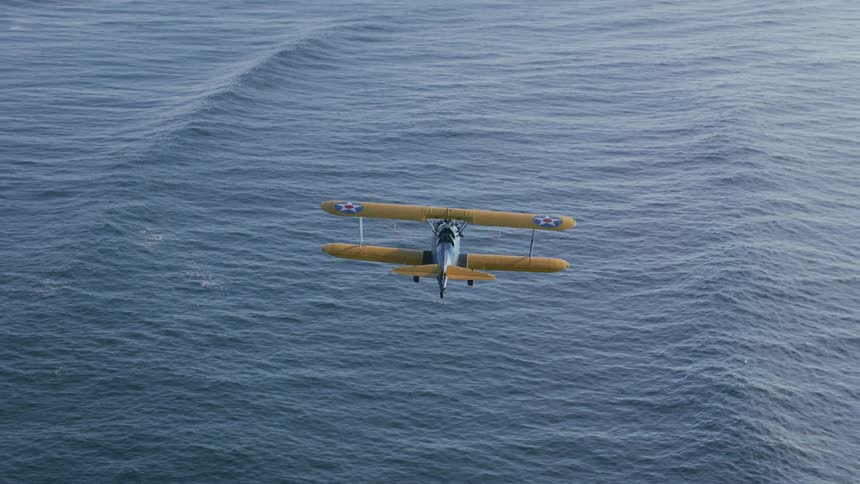 A person flies a biplane over the ocean during the day