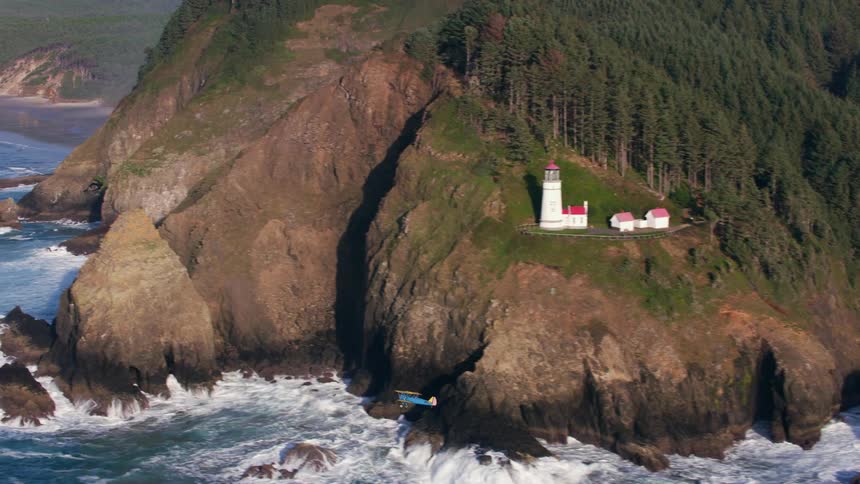 An airplane flies by the coast of land with a lighthouse