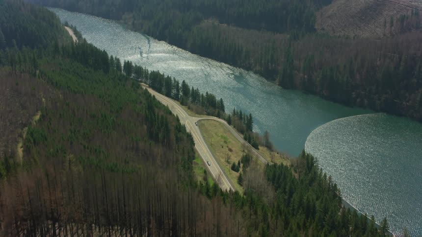 A river surface shimmers and ripples in the sunlight surrounded by trees and mountain slopes