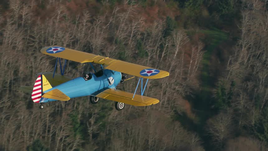 A small airplane flies over a forested mountain area