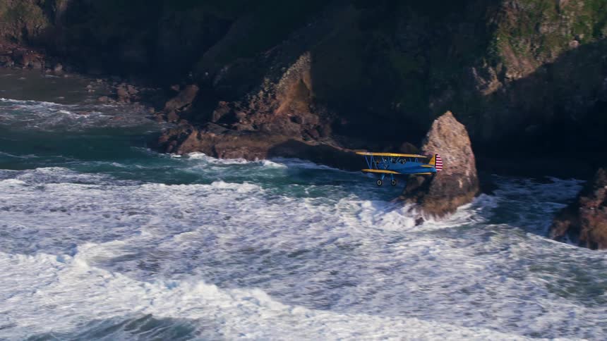 A small aircraft flies along a rocky steep coast