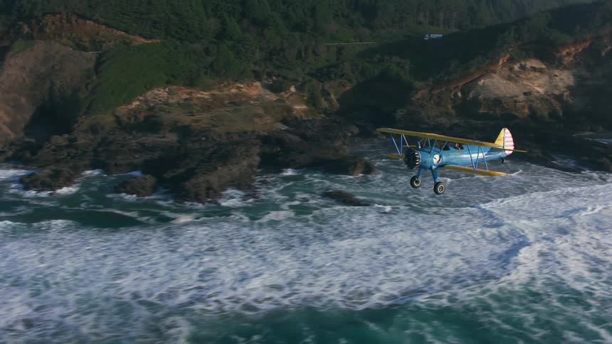 An airplane flies over a large body of water by the mountainside coastline