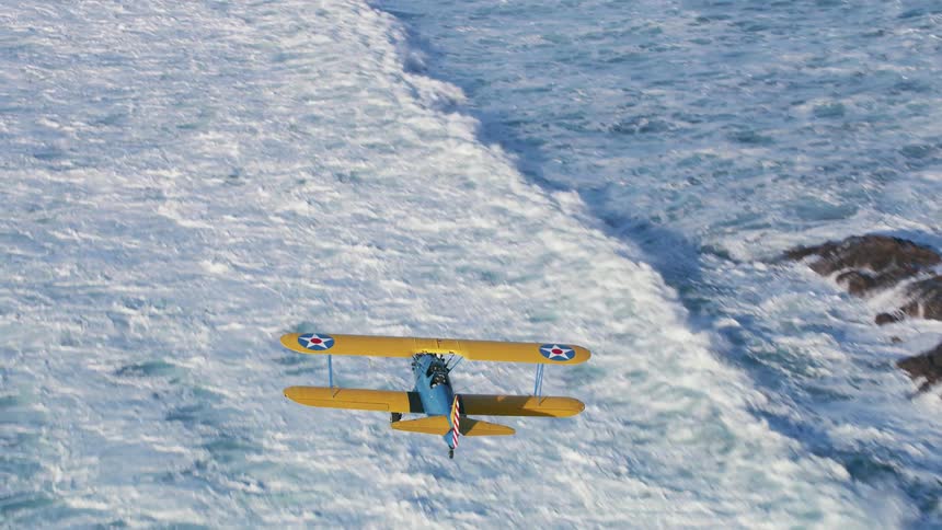 An airplane flies over a body of water near rocky land