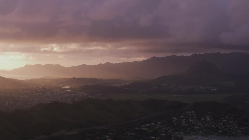 A city sprawls over the hilly and mountainous landscape under a thick layer of clouds